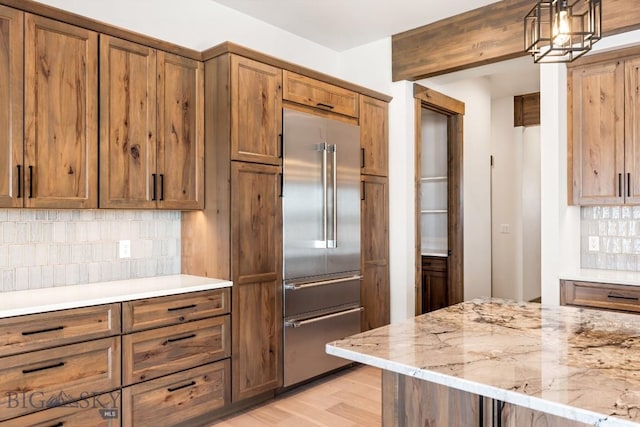 kitchen with light stone countertops, tasteful backsplash, stainless steel built in refrigerator, and brown cabinetry