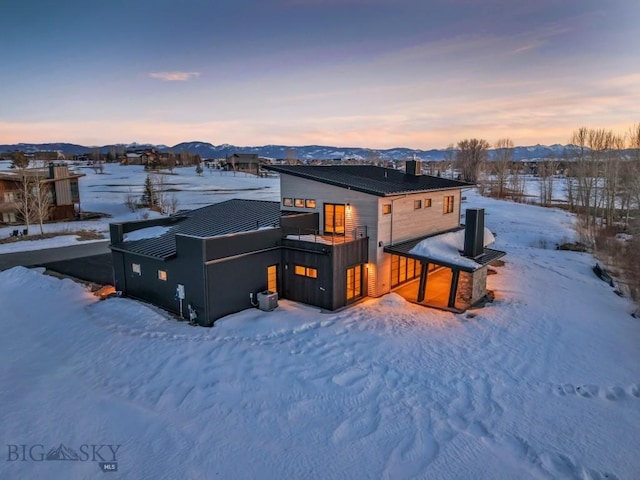 snow covered back of property featuring a chimney, a mountain view, metal roof, and a standing seam roof