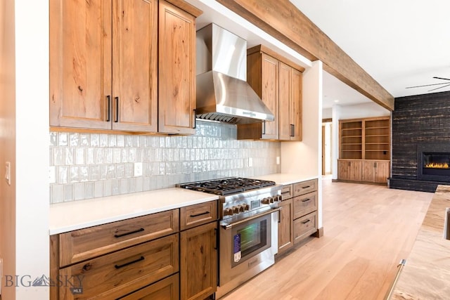 kitchen featuring a fireplace, high end stove, light countertops, light wood-style floors, and wall chimney exhaust hood