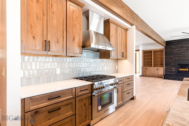 kitchen featuring light countertops, a fireplace, light wood-style flooring, high end stainless steel range oven, and wall chimney range hood