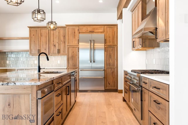 kitchen with pendant lighting, light wood-style flooring, high end appliances, wall chimney exhaust hood, and a sink