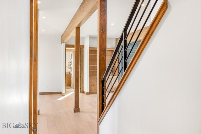 corridor featuring beamed ceiling, baseboards, light wood-style floors, and stairs