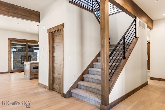 stairway with visible vents, baseboards, beamed ceiling, and wood finished floors