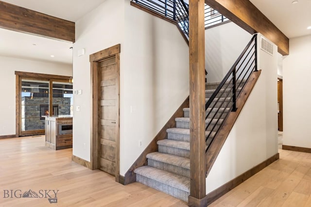stairway with baseboards, visible vents, wood finished floors, and beamed ceiling