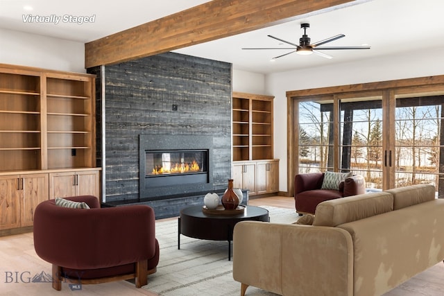 living area featuring a large fireplace, beam ceiling, light wood-style floors, and ceiling fan