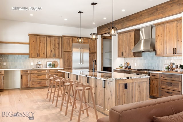 kitchen featuring brown cabinets, a sink, stainless steel appliances, a breakfast bar area, and wall chimney exhaust hood