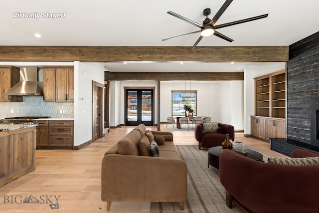 living area featuring beamed ceiling, a ceiling fan, a large fireplace, light wood finished floors, and baseboards