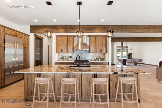 kitchen featuring beamed ceiling, a sink, built in fridge, wall chimney range hood, and backsplash