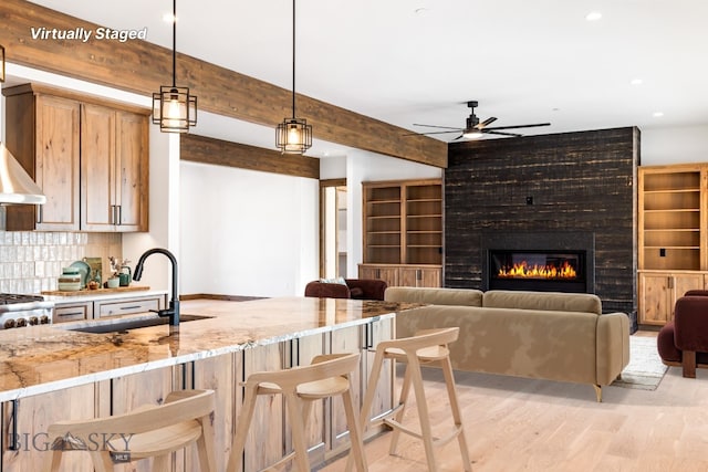 kitchen with a sink, a ceiling fan, tasteful backsplash, light wood-type flooring, and beamed ceiling
