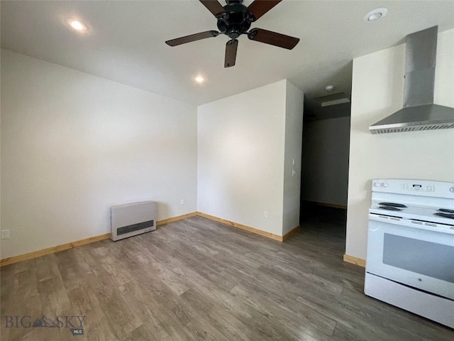 kitchen featuring ceiling fan, wall chimney range hood, wood finished floors, heating unit, and electric range