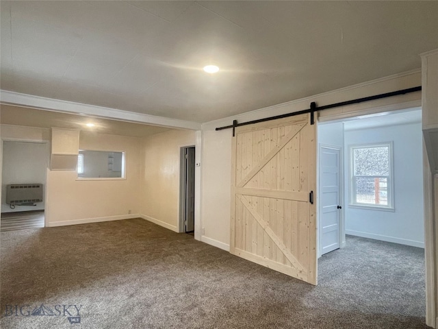 spare room with a barn door, heating unit, ornamental molding, and dark carpet