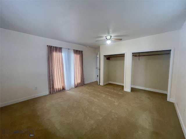 unfurnished bedroom featuring carpet flooring, a ceiling fan, baseboards, and two closets