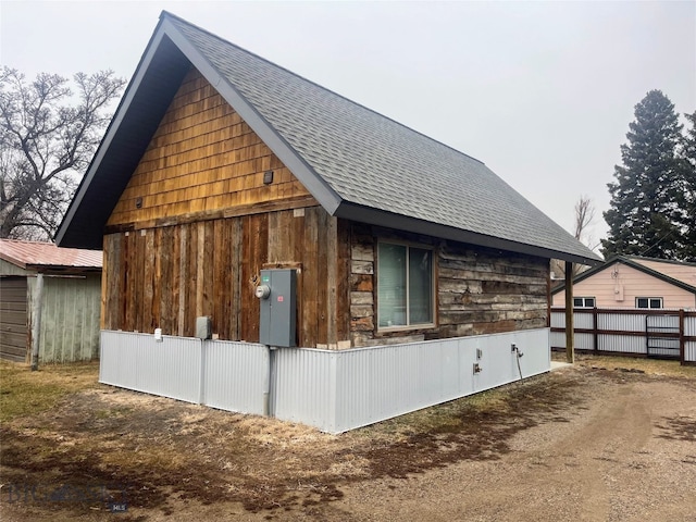 view of side of home with a shingled roof and fence