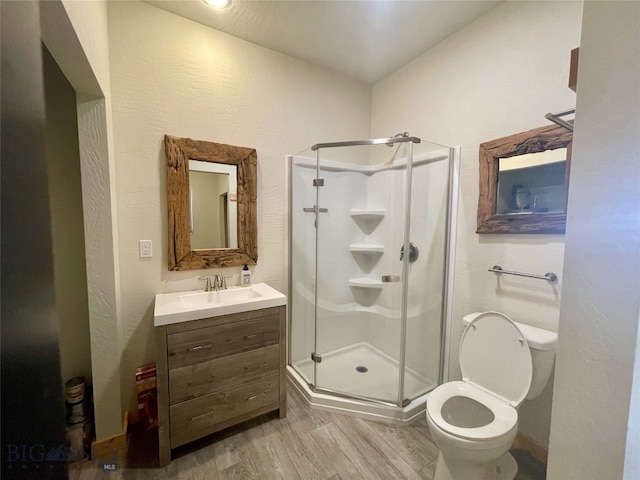 full bath with vanity, wood finished floors, a shower stall, and toilet