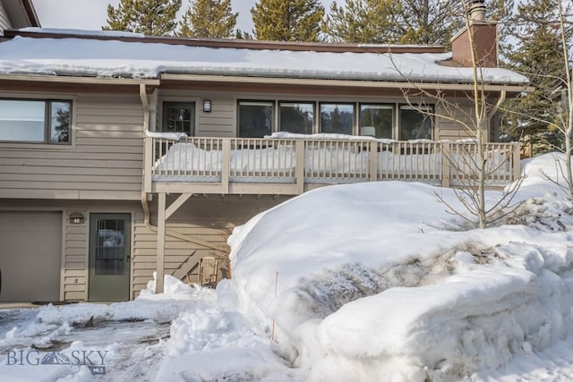 snow covered rear of property featuring an attached garage and a chimney