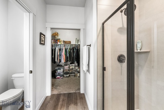 bathroom with wood finished floors, a spacious closet, toilet, and a stall shower