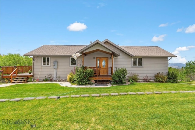 rear view of house featuring a deck, a shingled roof, and a yard