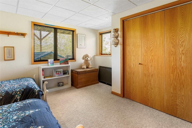carpeted bedroom featuring a drop ceiling, baseboards, and a closet