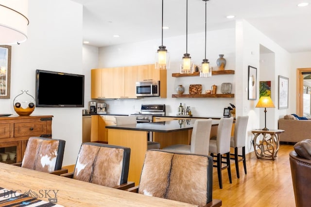 214 W Pine Cone Ter, Big Sky, MT 59716 - kitchen with appliances with stainless steel finishes, open floor plan, dark countertops, a kitchen island, and light wood-type flooring