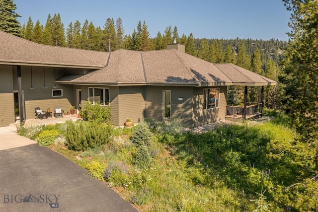 214 W Pine Cone Ter, Big Sky, MT 59716 - view of front of property with a balcony, board and batten siding, a patio area, a chimney, and a view of trees