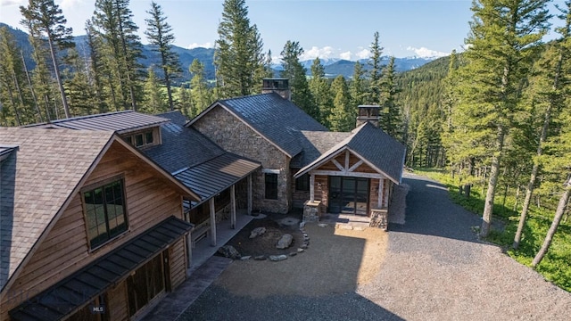 11310 Taiga Trl, Bozeman, MT 59715 - view of front of property featuring a wooded view, stone siding, a chimney, and a mountain view