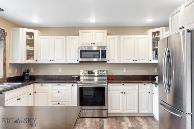 83 Sky Vw, Ennis, MT 59729 - kitchen featuring appliances with stainless steel finishes, dark countertops, glass insert cabinets, white cabinets, and light wood-style flooring