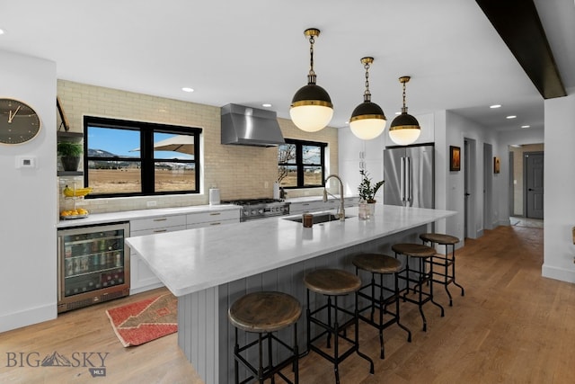 7980 Balsam, Bozeman, MT 59718 - kitchen featuring wall chimney range hood, beverage cooler, stainless steel appliances, light wood-style flooring, and white cabinetry