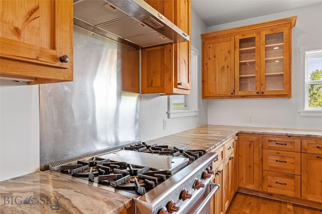 49 Wild Rye Pl, Three Forks, MT 59752 - kitchen featuring exhaust hood, stainless steel range with gas cooktop, glass insert cabinets, light wood-style flooring, and brown cabinets