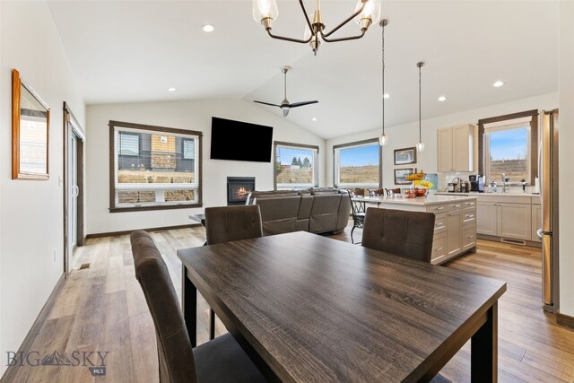 104 Albrey Trl Unit C, Bozeman, MT 59718 - dining area featuring a chandelier, light wood-type flooring, a warm lit fireplace, vaulted ceiling, and ceiling fan