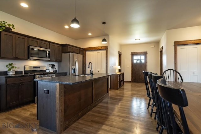 kitchen featuring dark brown cabinets, a sink, dark wood-type flooring, a center island with sink, and stainless steel appliances