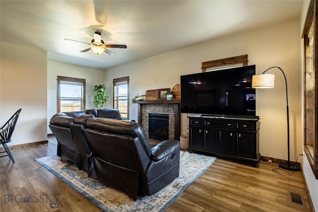 living room with a ceiling fan, baseboards, visible vents, wood finished floors, and a fireplace