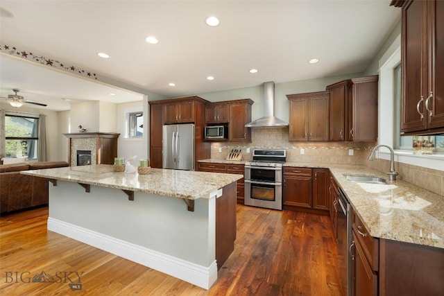 2026 Southbridge, Bozeman, MT 59718 - kitchen featuring appliances with stainless steel finishes, wall chimney range hood, a sink, a kitchen breakfast bar, and open floor plan