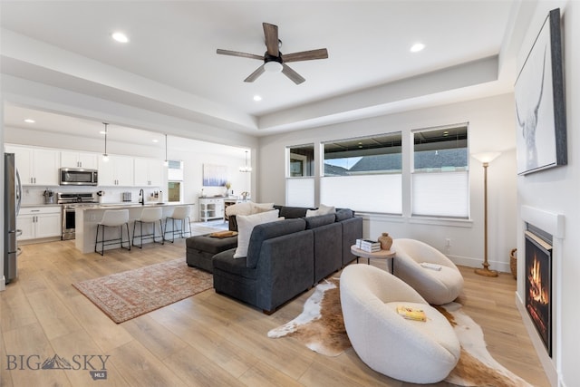 1502 Cyril Way, Belgrade, MT 59714 - living area featuring ceiling fan, a lit fireplace, light wood finished floors, a tray ceiling, and recessed lighting
