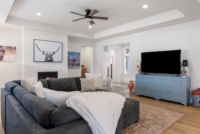 1502 Cyril Way, Belgrade, MT 59714 - living area with a tray ceiling, a ceiling fan, light wood-style floors, a glass covered fireplace, and recessed lighting