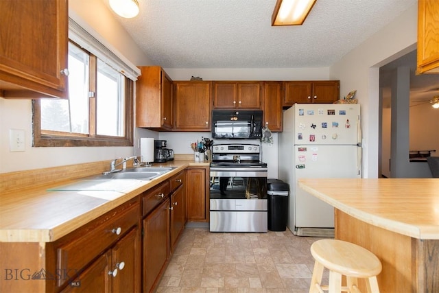 kitchen featuring light countertops, stainless steel electric range, a sink, freestanding refrigerator, and black microwave