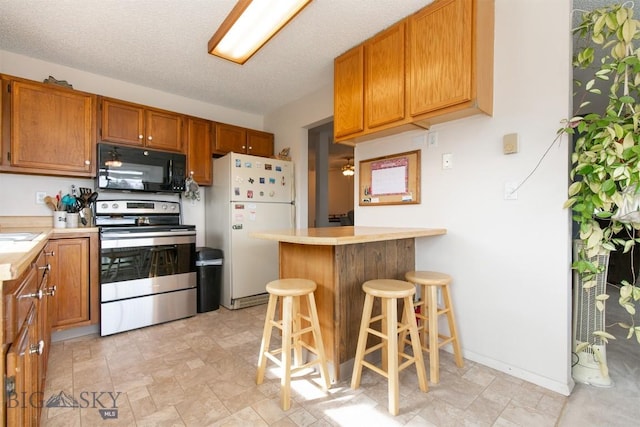 kitchen featuring light countertops, stainless steel electric range, freestanding refrigerator, a peninsula, and black microwave