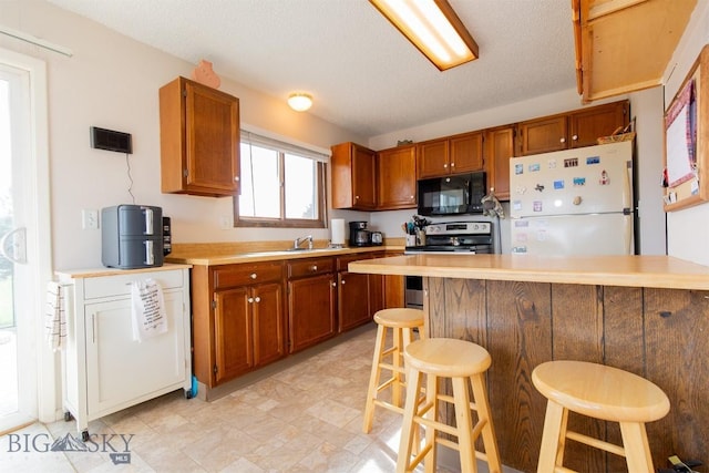 kitchen with light countertops, brown cabinets, stainless steel electric range, black microwave, and freestanding refrigerator