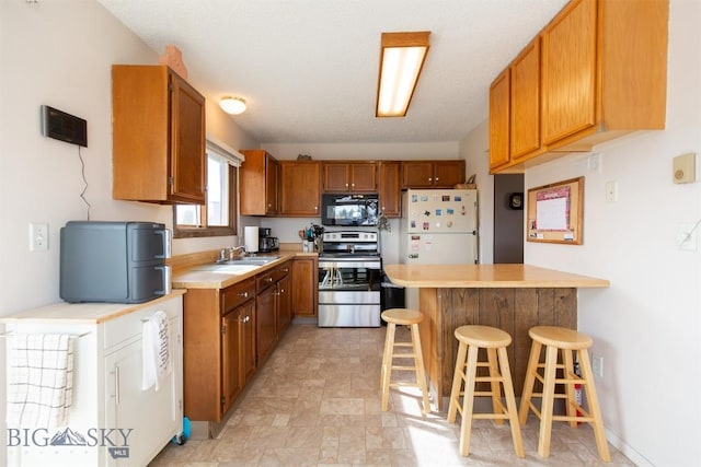 kitchen with a peninsula, a sink, black microwave, stainless steel electric stove, and freestanding refrigerator