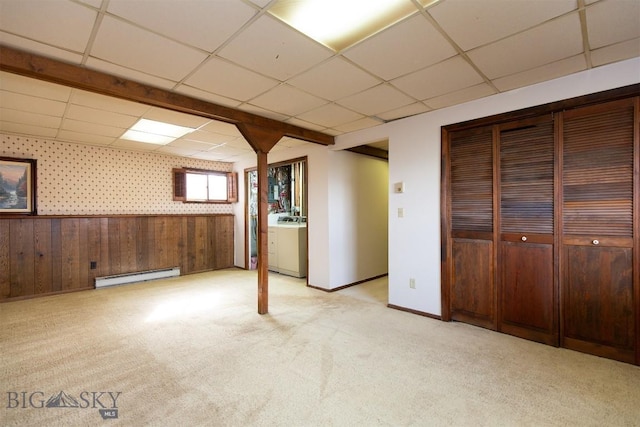 below grade area featuring wallpapered walls, baseboard heating, light carpet, a paneled ceiling, and washer / dryer