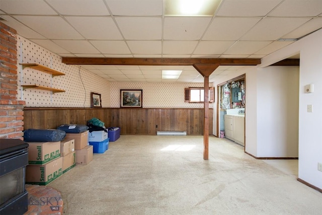 basement with a baseboard heating unit, a wood stove, carpet flooring, wallpapered walls, and wainscoting