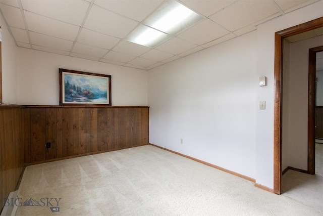 unfurnished room with a drop ceiling, a wainscoted wall, wooden walls, and light colored carpet