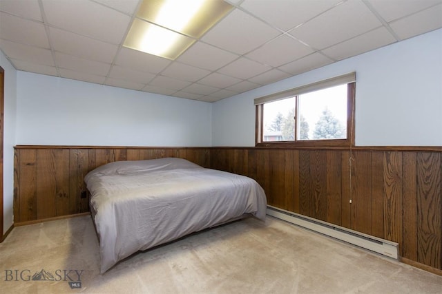 carpeted bedroom featuring a wainscoted wall, baseboard heating, wooden walls, and a drop ceiling
