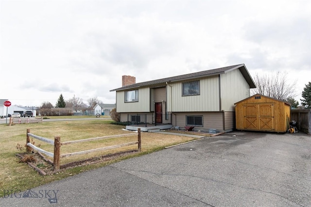 split foyer home with driveway, a shed, a chimney, an outbuilding, and fence