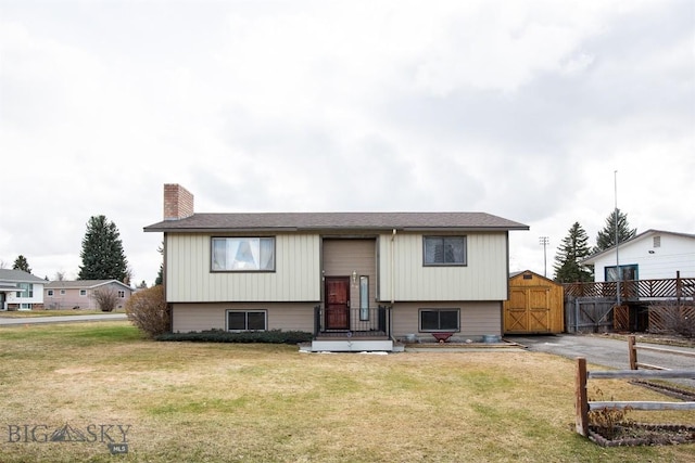bi-level home with fence, a storage shed, a chimney, a front lawn, and an outdoor structure