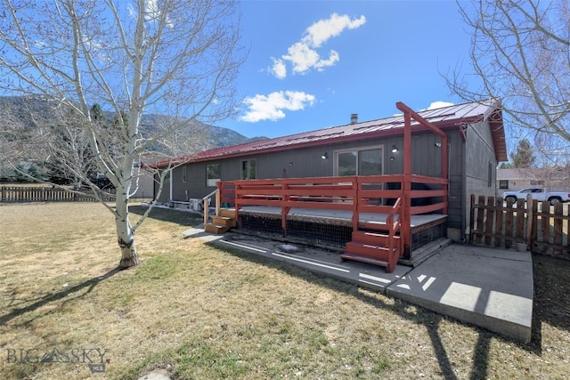 back of property featuring a deck with mountain view, a lawn, metal roof, and fence