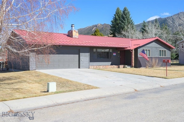 single story home with concrete driveway, an attached garage, a front lawn, metal roof, and a mountain view