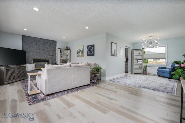 living area with an inviting chandelier, baseboards, a textured ceiling, a stone fireplace, and wood finished floors