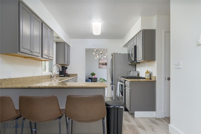 kitchen featuring a peninsula, a kitchen bar, stainless steel appliances, a sink, and gray cabinets