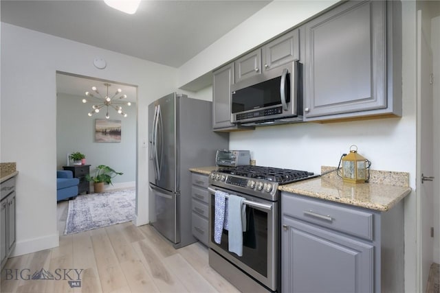 kitchen with light wood-style flooring, a chandelier, light stone countertops, stainless steel appliances, and gray cabinets