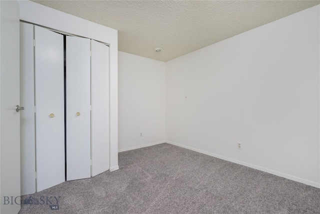 unfurnished bedroom with a closet, carpet floors, a textured ceiling, and baseboards